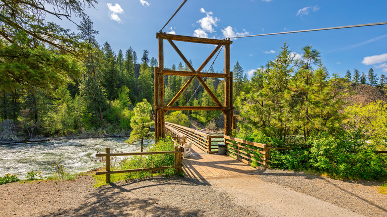 Wood pedestrian bridge crosses forest river in Spokane, Washington