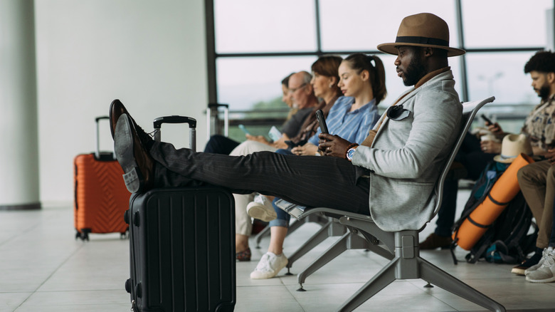 A man sitting at an airport with his feet on his luggage