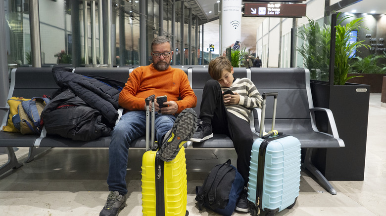 A man and a child sitting at an airport with luggage in front of them and on the seats next to them