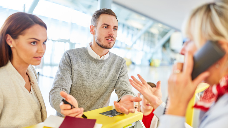 A frustrated couple talking to an airport agent who is on the phone