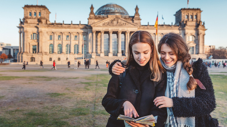 Woman smiling with arm around second woman as they both read a map in front of Berlin's Reichstag Building