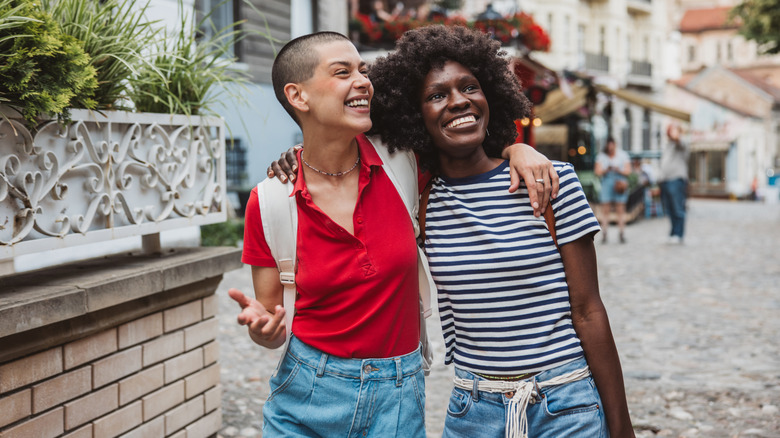 Two women smiling and walking with arms around each other through a European street