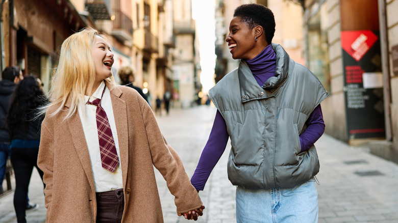 Two women laughing together as they walk through the streets of Barcelona holding hands