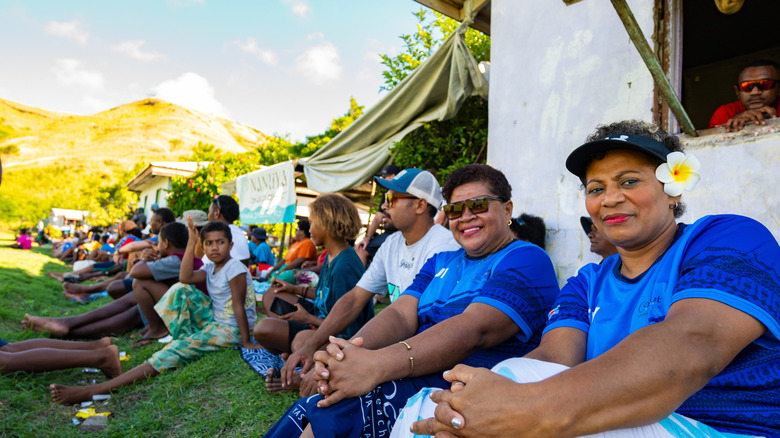 Samoan people by a white building sitting on the ground