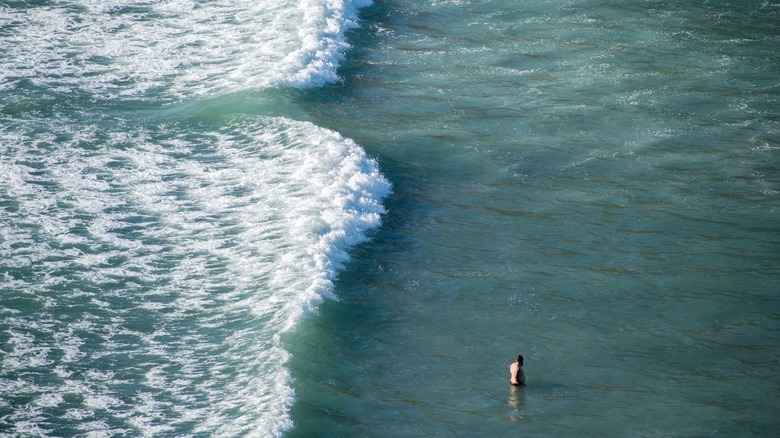 A lone swimmer standing in the surf next to a dangerous rip current