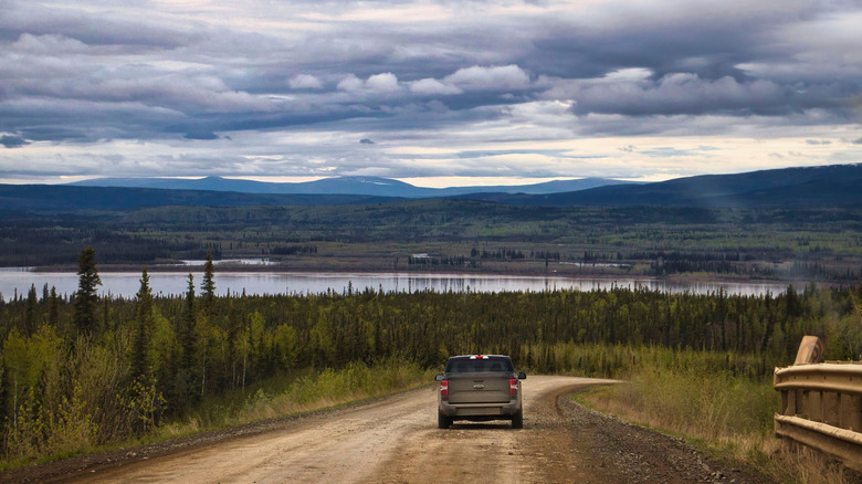 A truck on a dirt road with clouds and mountains in the background on the Dalton Highway, Alaska