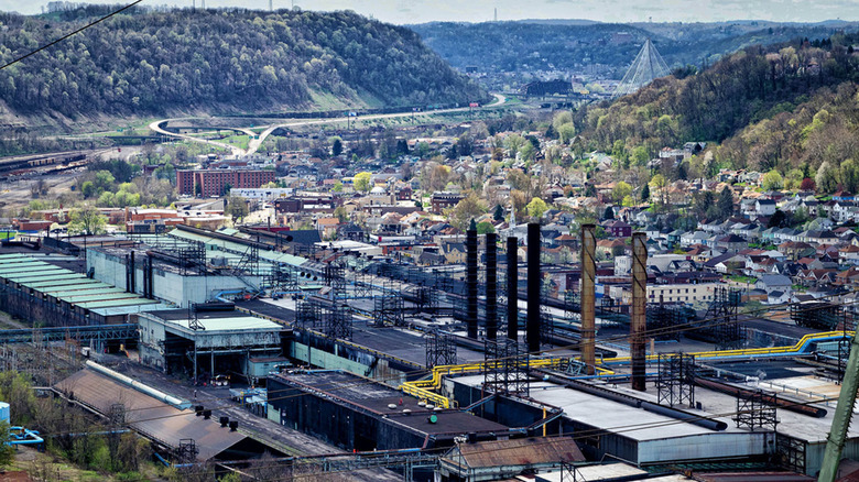 Aerial view of Weirton, West Virginia, with an industrial plant in the foreground of homes and buildings, with treed hills and bridges in the background