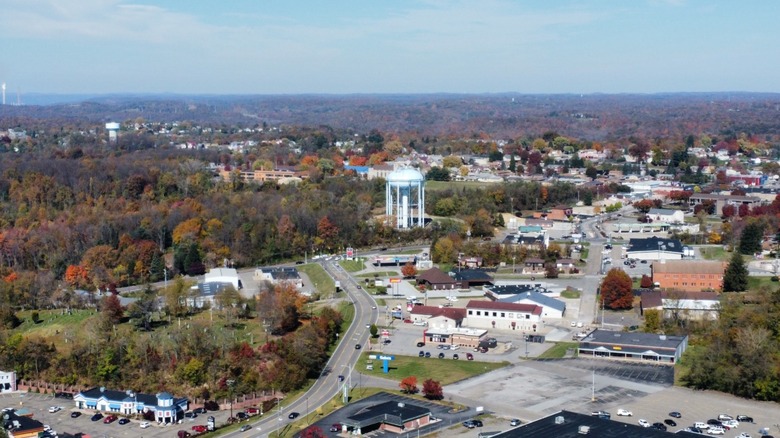 Aerial view of Weirton, with a blue water tower surrounded by autumn trees and businesses, with homes and hills in the background under a blue sky