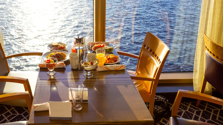Chairs and a dining table set with breakfast inside a cruise dining room overlooking the water