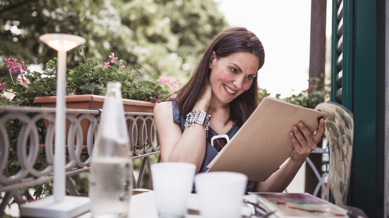 A woman smiles while studying the menu of an outdoor sit-down restaurant in Italy
