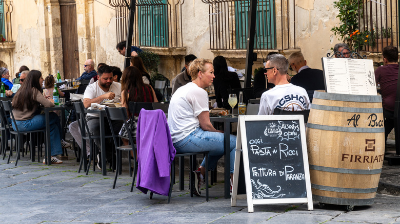 Customers are seated outside, dining streetside, at a restaurant in Italy