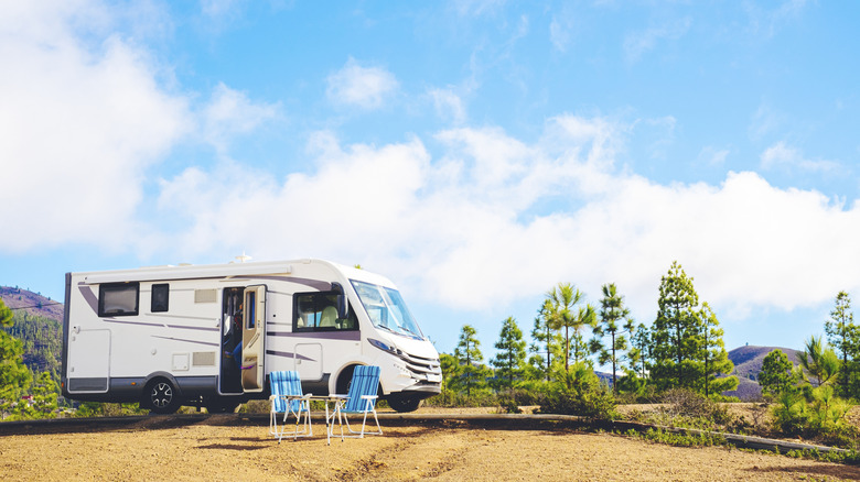 RV parked up at deserted site near trees, with two chairs out front
