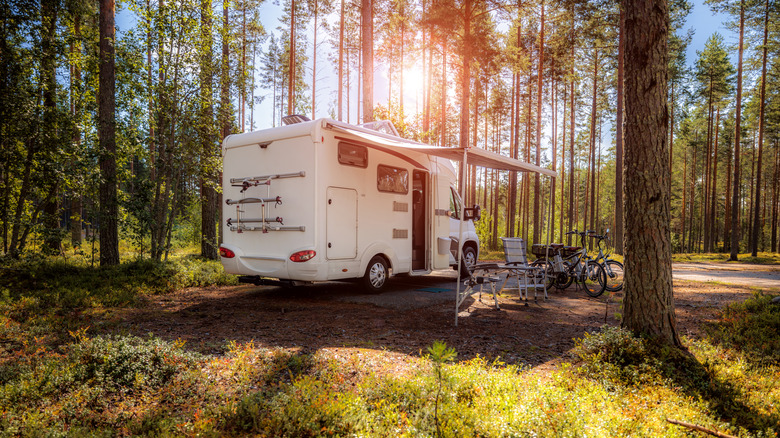 RV parked in forest with awning covering chairs and bikes