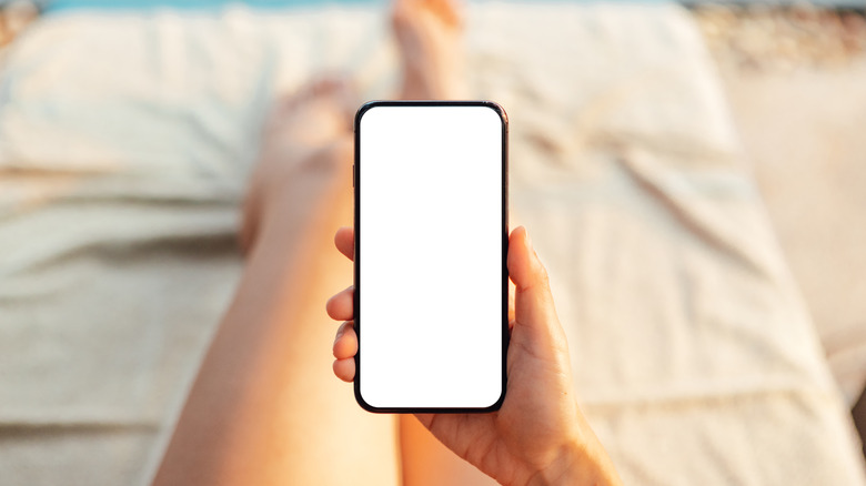Close-up of young woman holding smart phone while relaxing at poolside