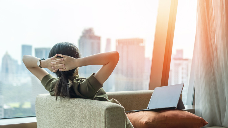 Women relaxes in a chair with a laptop in her lap overlooking skyscrapers