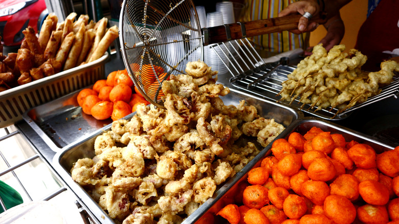Street food vendor transferring freshly fried squid into a pan.