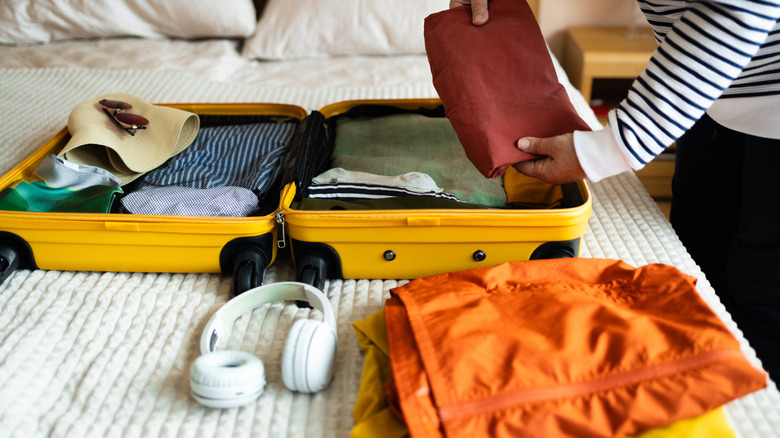 A person packs a yellow suitcase for travel