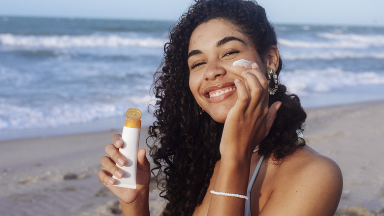 A smiling woman applies sunscreen on a beach