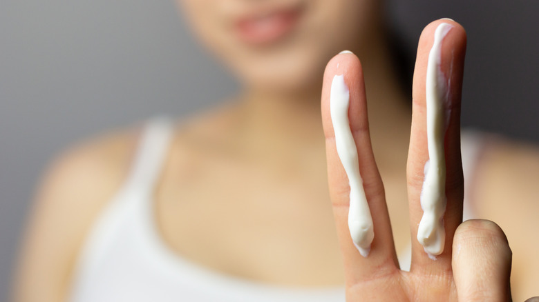 A woman raises two sunscreen-covered fingers close to the viewer