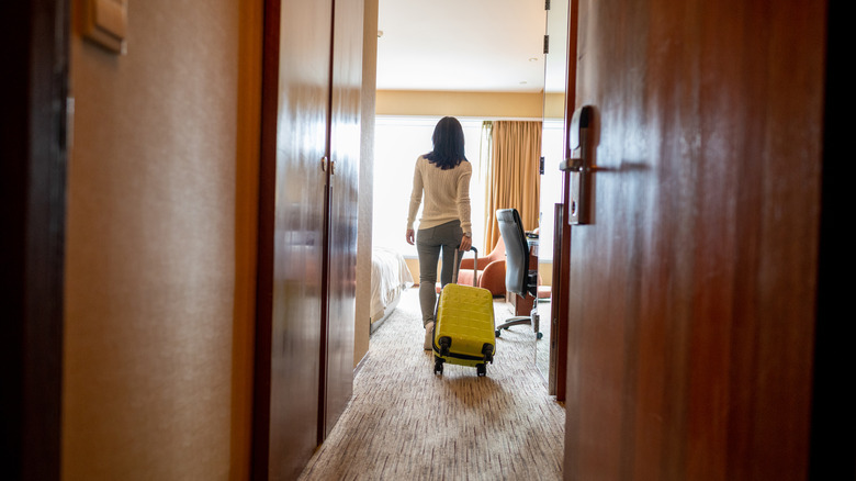 Person entering a hotel room with a suitcase