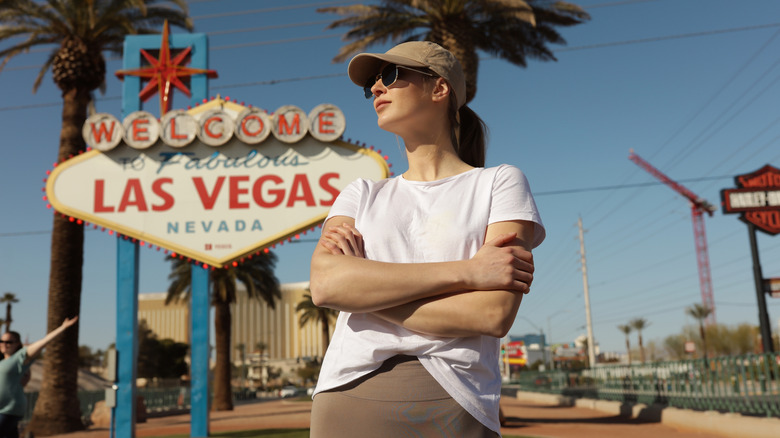 A woman in sunglasses and cap stands in front of the iconic 