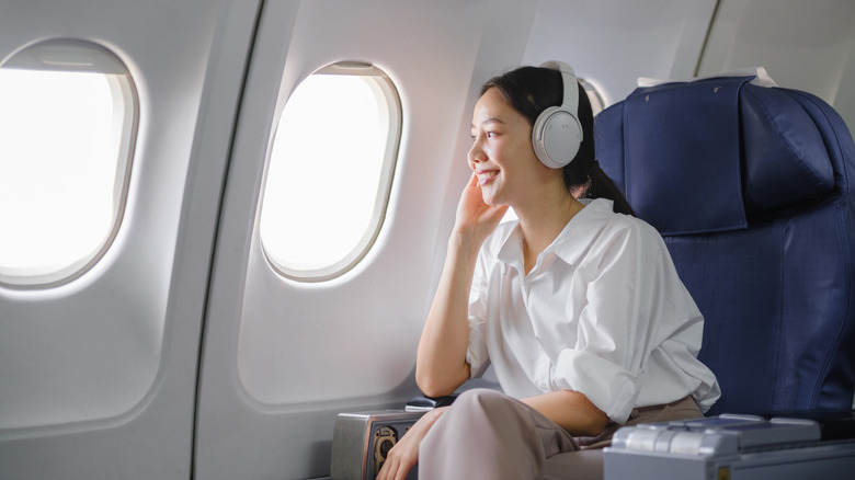 Woman with headphones looking out the window of an airplane
