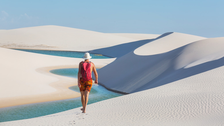Male hiker with red backpack walking on the white gympum dunes