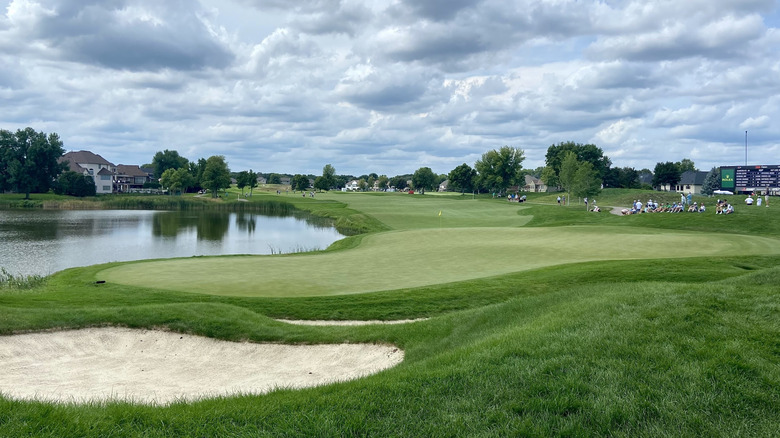 The TPC Twin Cities golf course, with hills, a pond and a few spectators, in Blaine