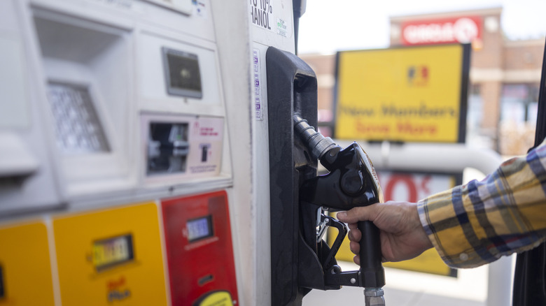 A hand grips the nozzle at a gas pump