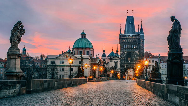 Iconic Charles Bridge in Prague at sunrise with historical statues, cobblestone path, and a vibrant sky,