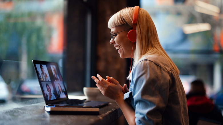 Close up shot of a young woman wearing glasses and headphone is sitting in the cafeteria having a video meeting and while looking down at the screen.