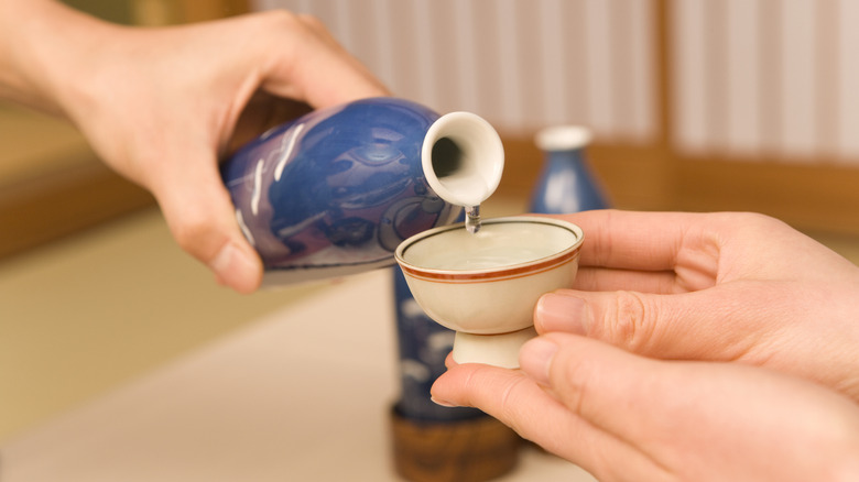 Sake being poured from a bottle into a cup in someone's hands.