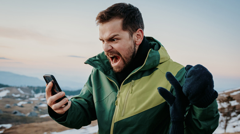 Man in a jacket screaming into his phone on a hike