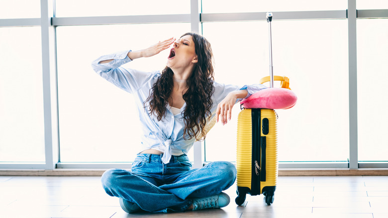 Woman with her luggage sitting on the airport floor and yawning