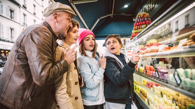 People pointing at macarons in a shop window