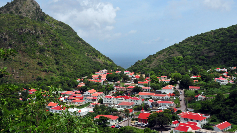 Red-roofed houses cluster together between tropical hills on the island of Saba