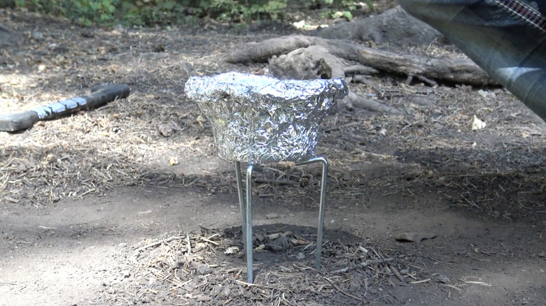 Tinfoil bowl on makeshift camp stove made of tent pegs