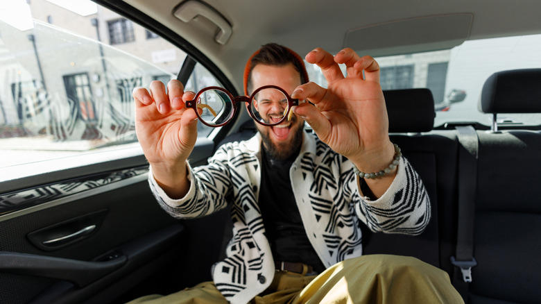 A casually dressed man holding out his glasses and smiling
