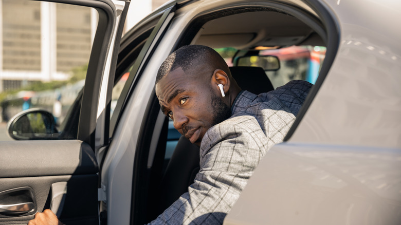 A businessman wearing earphones getting out of a gray car looking backwards