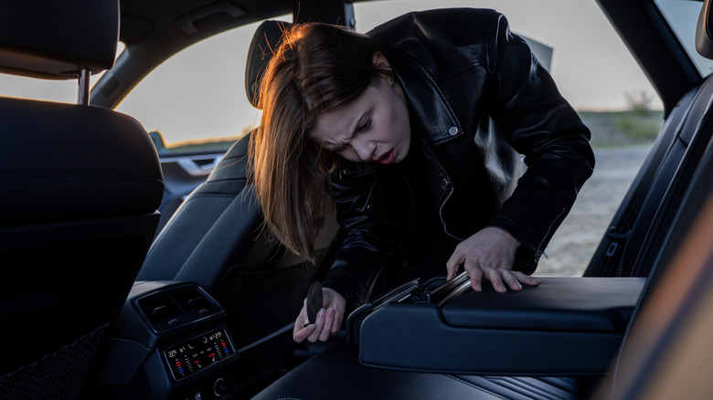 A worried woman in black leather jacket searching the back seat of a car