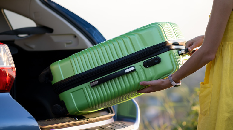 Woman in yellow dress putting a green luggage into the trunk of a blue car