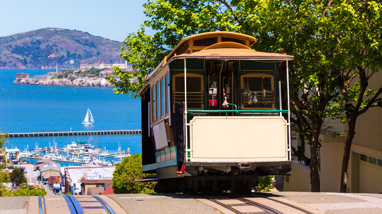 A cable car rising up a hill with the San Francisco Bay behind