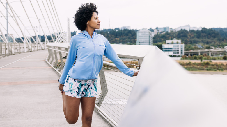 an african american woman prepares for exercise with a leg stretch while looking out over a bridge across the columbia river in portland, oregon