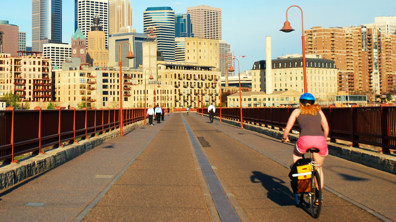 person on a bicycle riding along a multi-use trail bridge with the minneapolis skyline in the background