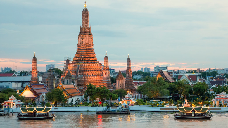 Traditional boats on the Chao Phraya River with Wat Arun in the background at sunset in Bangkok, Thailand