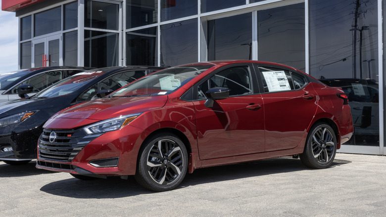 A red Nissan Versa waits in the parking lot of a dealership