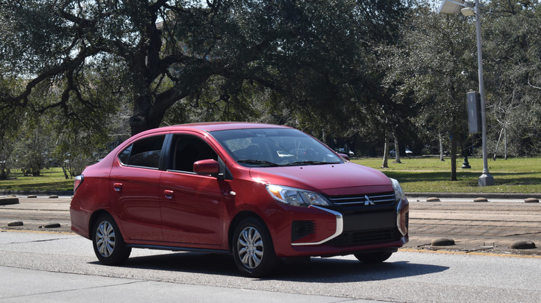 A red Mitsubishi Mirage drives past a quiet green park