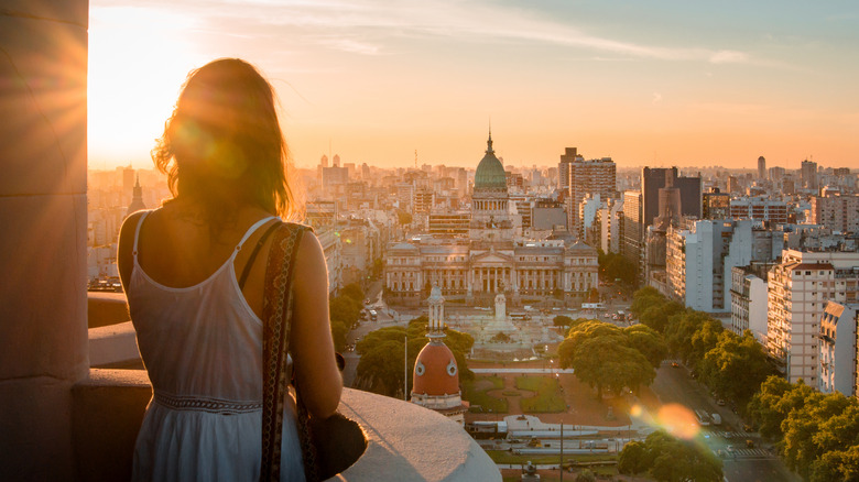A woman stands on a balcony at sunset overlooking the city of Buenos Aires