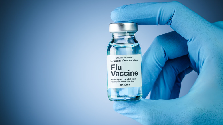 Hand in blue medical gloves holding a vaccine bottle with flu vaccine text