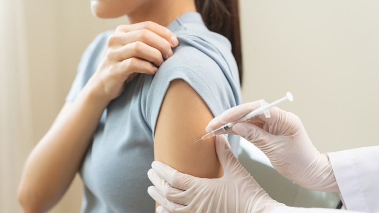 Nurse wearing surgical gloves and holding a hypodermic needle giving a vaccine to a young woman